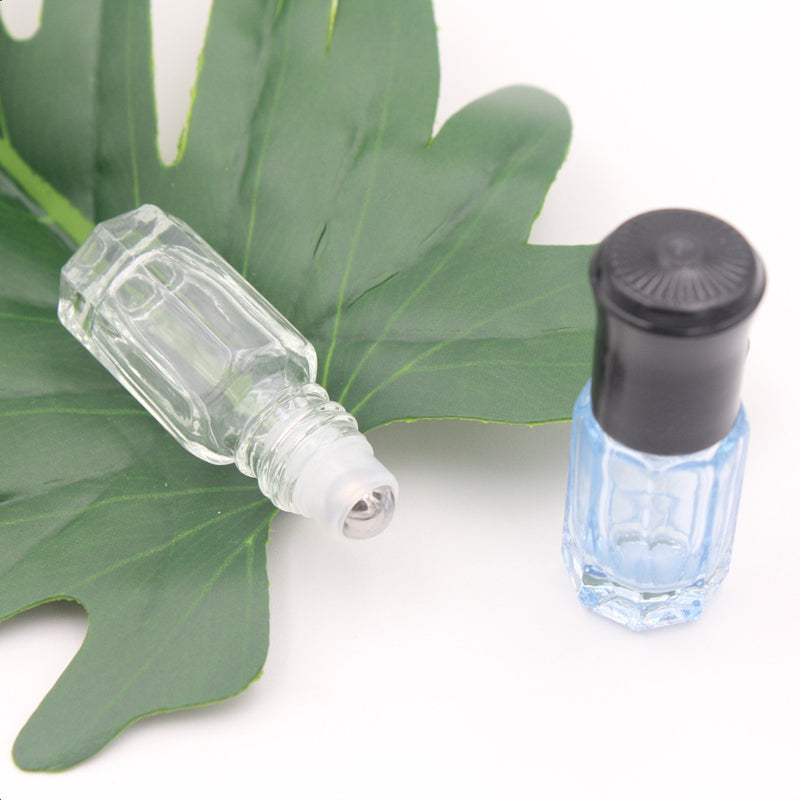 Colorful 3ml and 6ml glass essential oil roller bottles with stainless steel balls on a green leaf.