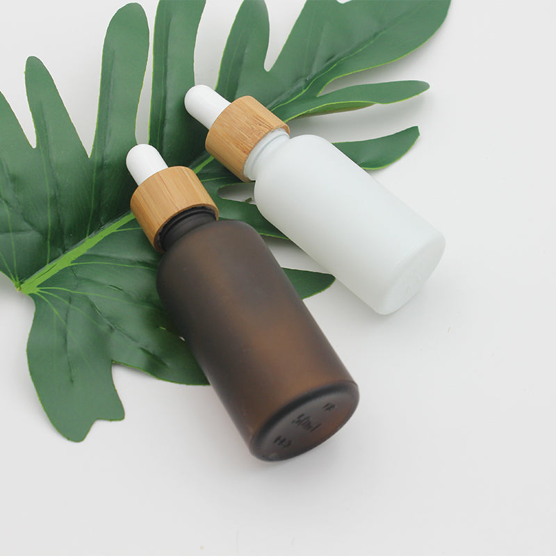 Frosted glass dropper bottles in amber and white with bamboo caps, displayed on a green leaf.