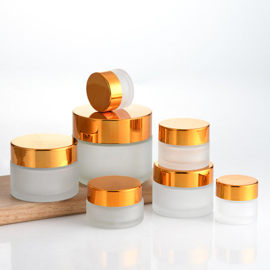 Frosted glass cosmetic jars in various sizes with gold lids, ideal for storing creams and cosmetics.